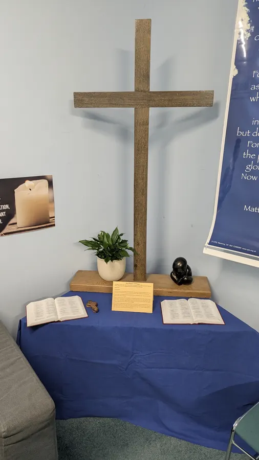 A plain wooden cross above a table draped in blue with two open Bibles