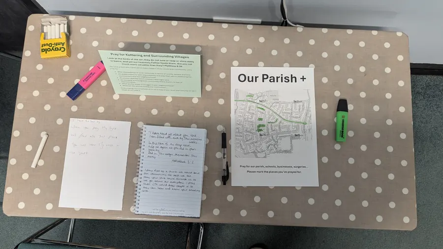 The parish prayer table from above: map, notebook, highlighters and chalk on a spotted tablecloth