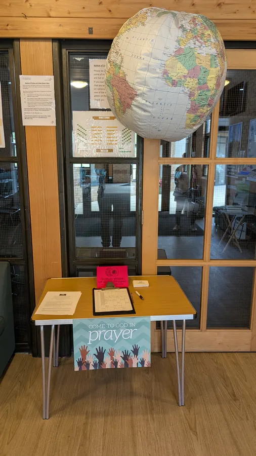 A welcome table under a hanging inflatable globe, with a sign reading Come to God in prayer